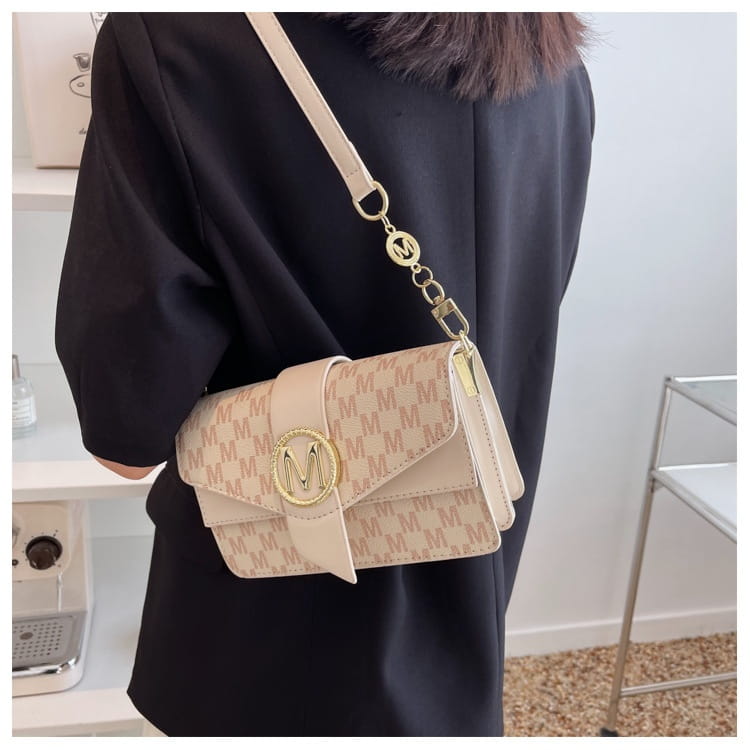 Beige monogram letter print crossbody messenger bag featuring a repeating m pattern and gold-tone circular logo clasp.