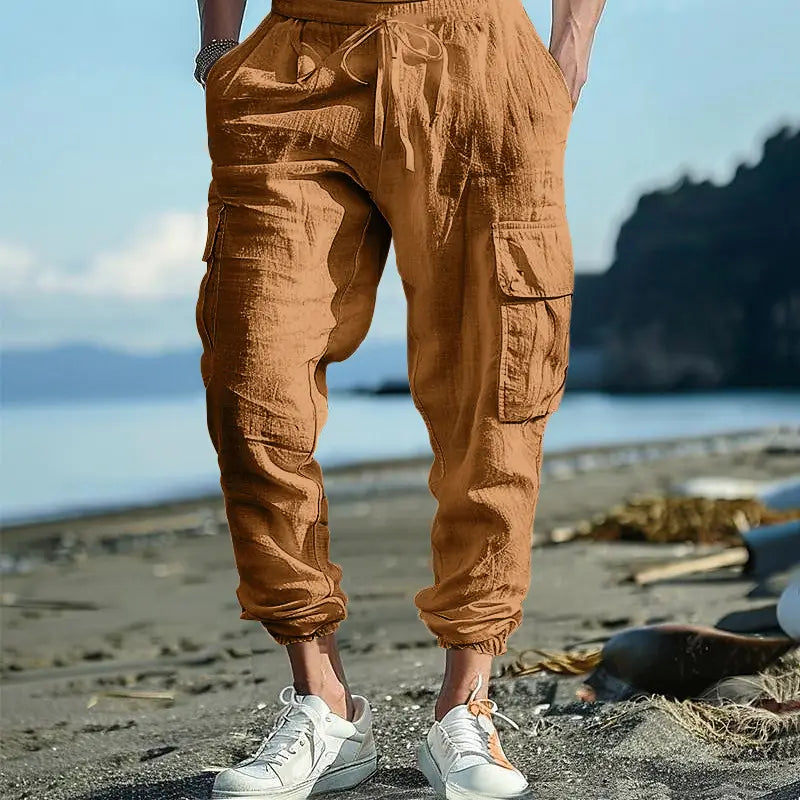 Men linen cargo pants in tan with a drawstring waist and multiple pockets designed for a cuffed ankle fit.
