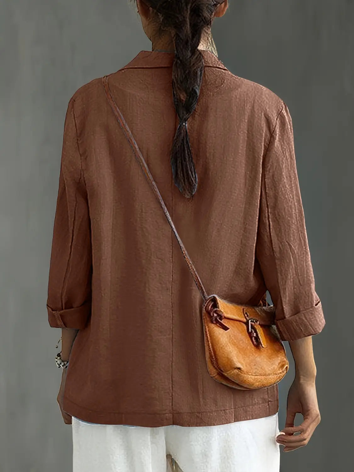Un bolso cruzado de cuero color camel con cierre de cordón y correa ajustable, mostrado junto con un blazer de lino para mujer, casual y de trabajo.