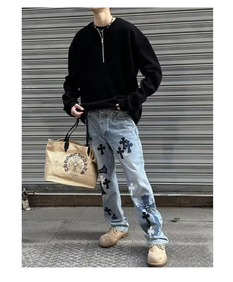 Jeans de mezclilla de lavado claro con parches cruzados negros y un diseño de parches tipo patchwork desgastado, mostrado desde el lado posterior en una imagen de producto de una sudadera tipo jersey acanalada de media cremallera para hombre.