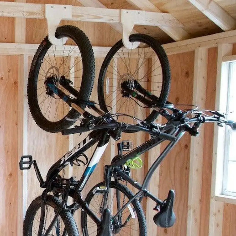 Heavy duty ceiling mount vertical bicycle storage hooks holding black mountain bikes with blue and white accents on wooden wall in rustic shed