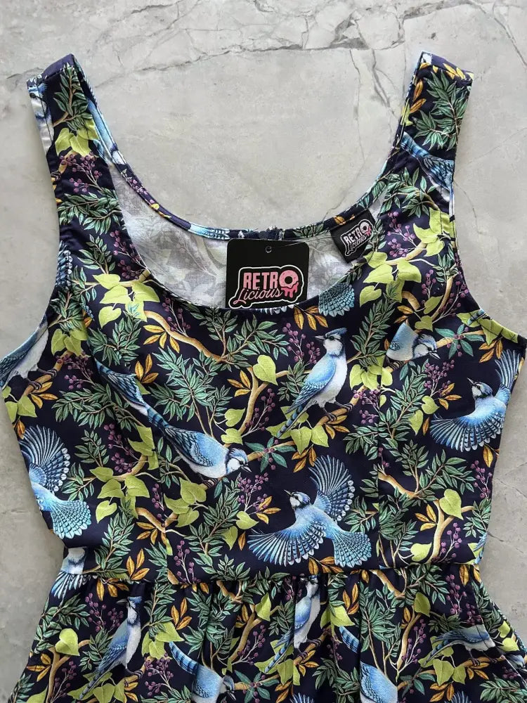 A navy blue sleeveless cotton fit and flare midi dress with a vibrant blue jay and foliage print