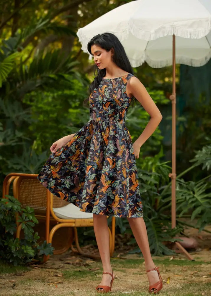 A woman wears a birds of a feather vintage 1950s cotton midi dress with dark navy and vibrant tropical leaf patterns
