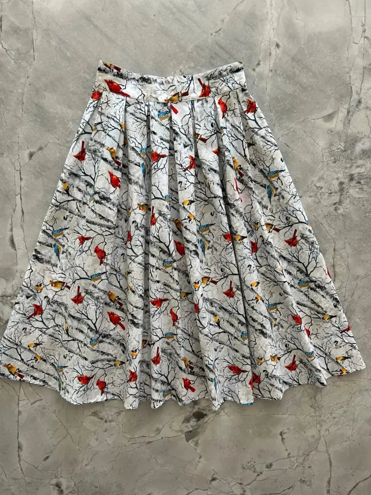 A white vintage pleated cotton skirt with pockets featuring a vibrant red cardinals and birds pattern on black branches