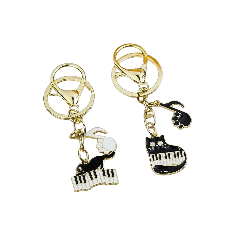 Gold-toned keychains with black and white enamel cat charms playing piano and musical notes for music lovers