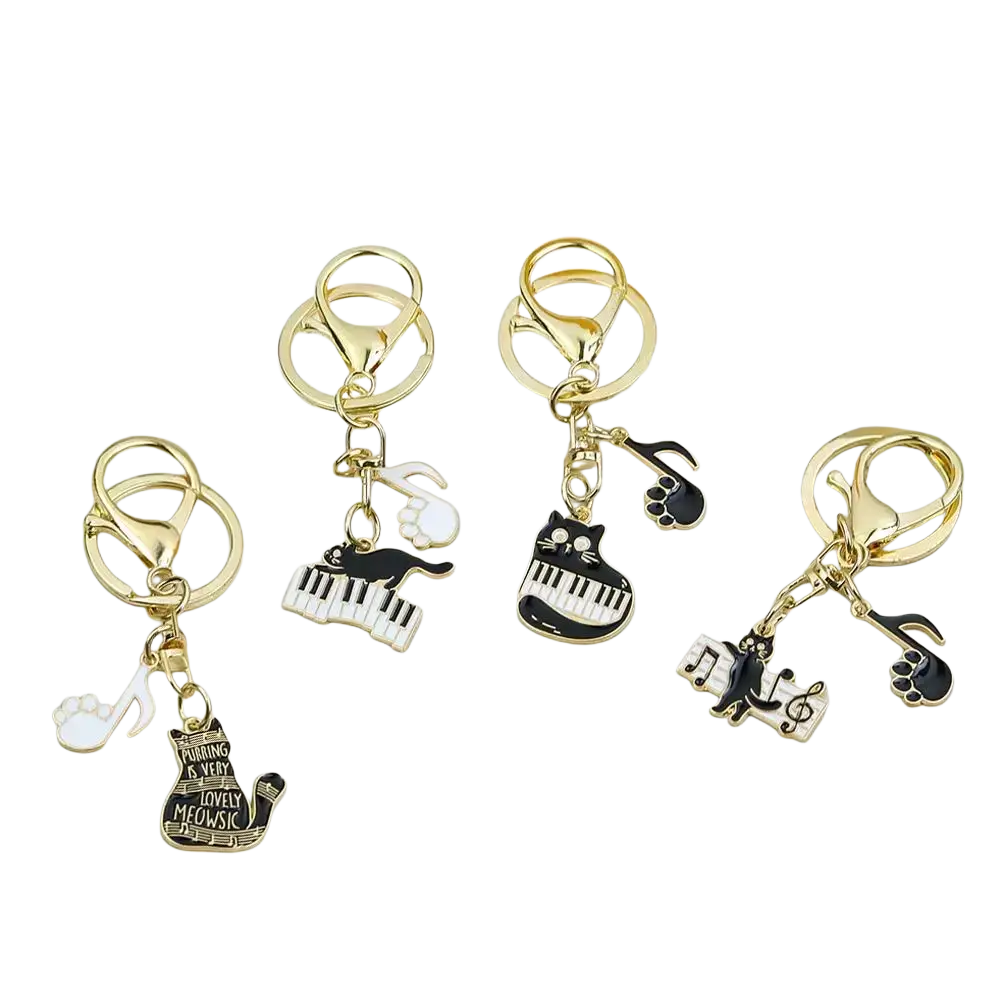 Gold-toned keychains with black and white enamel cat designs featuring piano keys musical notes and paw prints