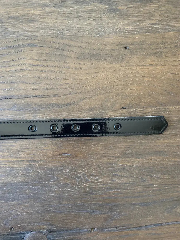 Retro black patent vinyl belt featuring five silver-toned eyelets and a pointed end in sleek patent leather