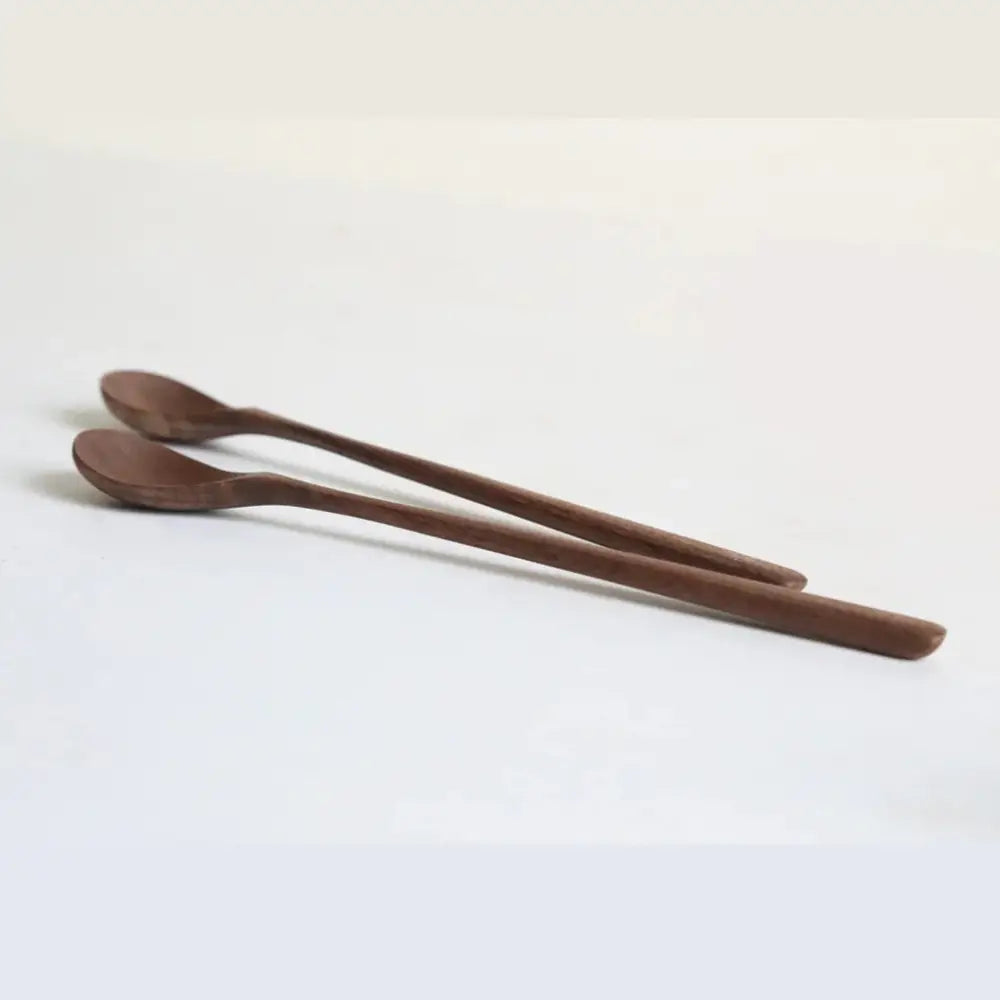 Two slender dark brown handcrafted black walnut wood dining spoons with smooth polished surfaces on white background