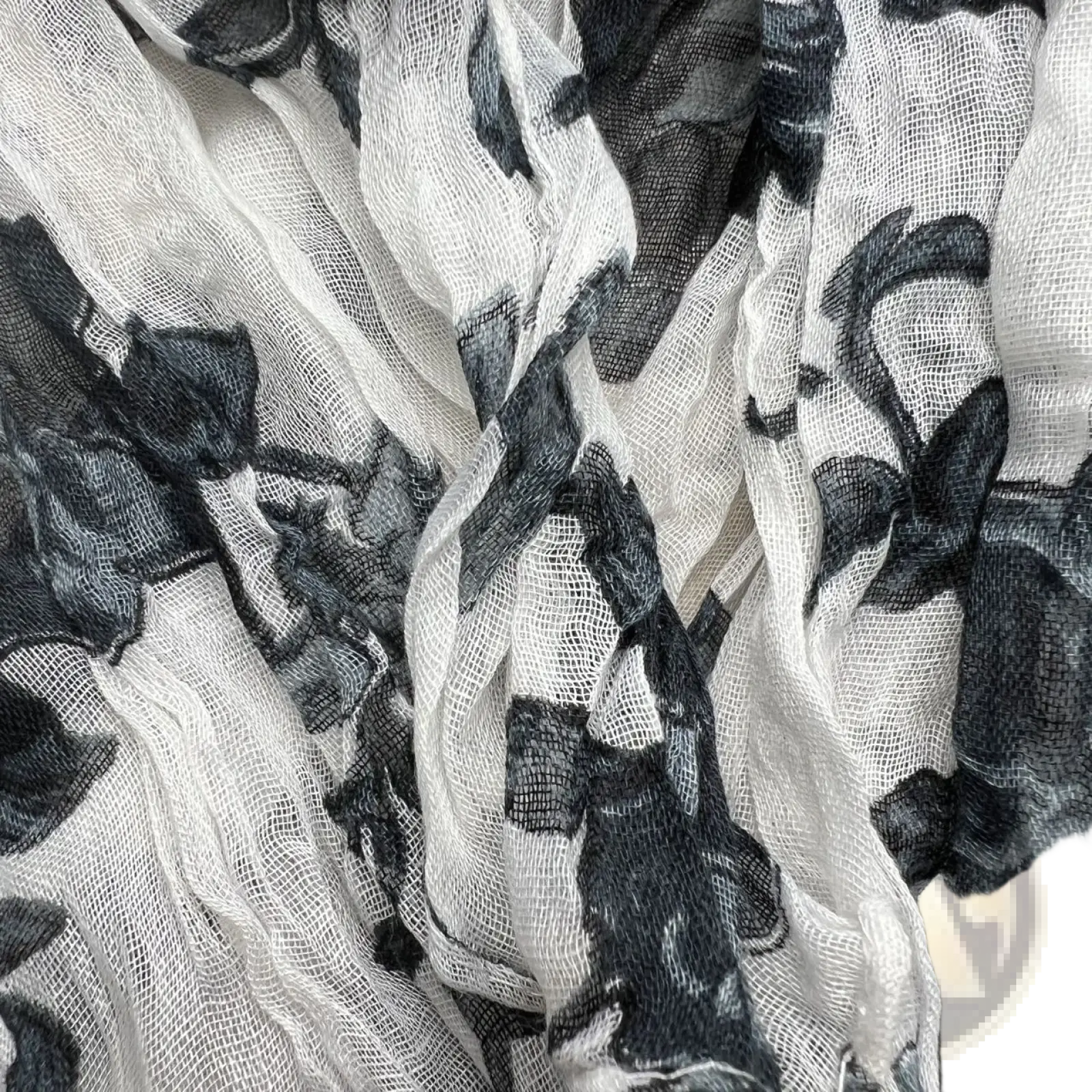 A delicate white chiffon scarf with bold black floral pattern featuring soft flowing folds in crinkle style