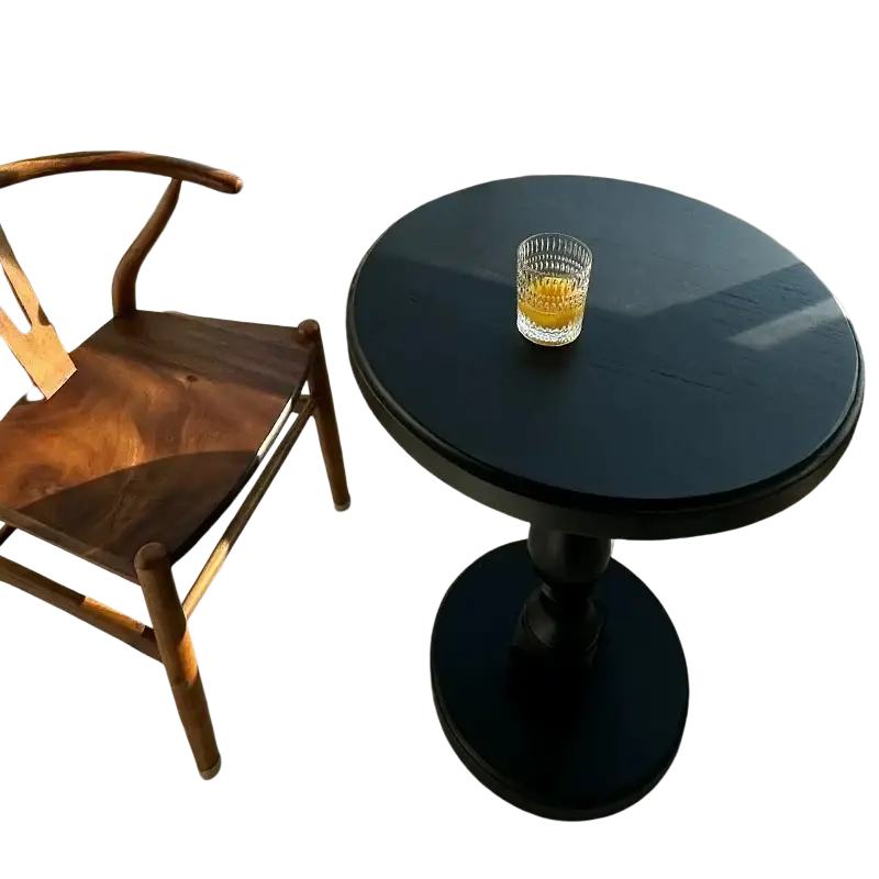 Black wooden pedestal round accent table with a glass of amber liquid on top on a black round surface