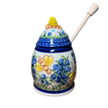 A white ceramic honey pot hand-painted with blueberries bees floral patterns with matching lid and cream-colored dipper