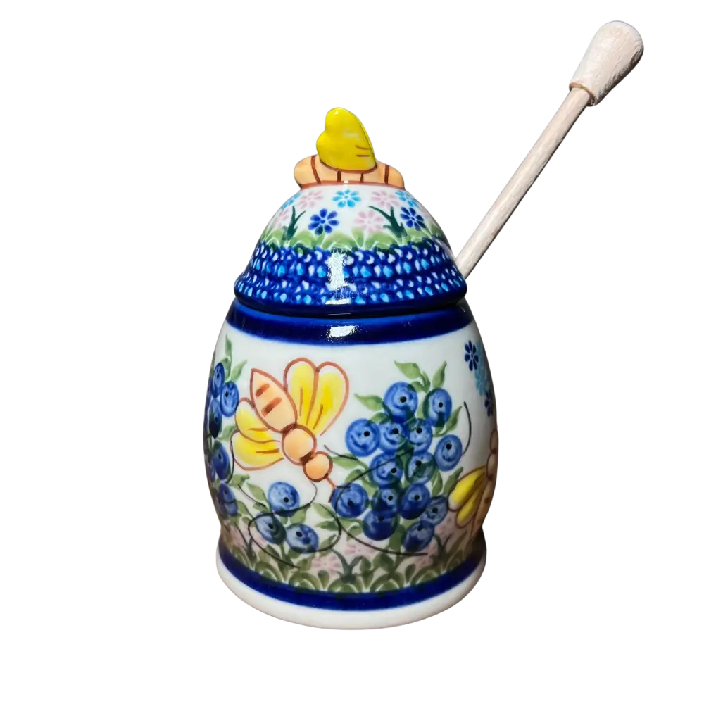A white ceramic honey pot hand-painted with blueberries bees floral patterns with matching lid and cream-colored dipper