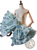 A delicate light blue floral bridal dress with a voluminous ruffled skirt and matching oversized bow at the shoulder