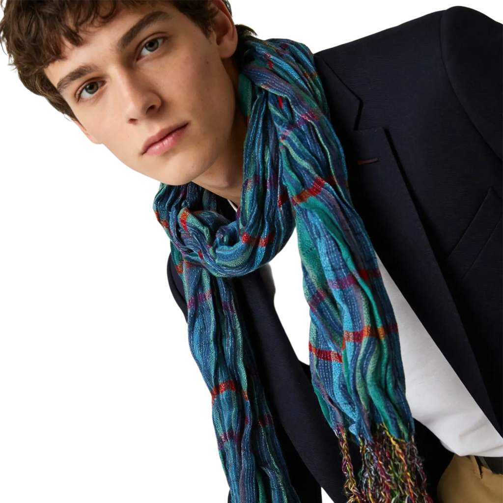 A blue jacquard textured winter scarf in shades of blue and green with red and purple stripes and multicolored fringe