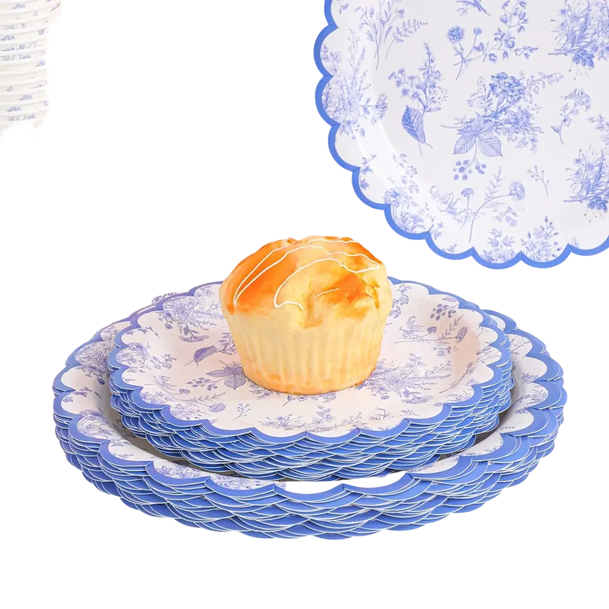 A golden-brown cupcake with white icing on a stack of blue and white floral porcelain party tableware plates