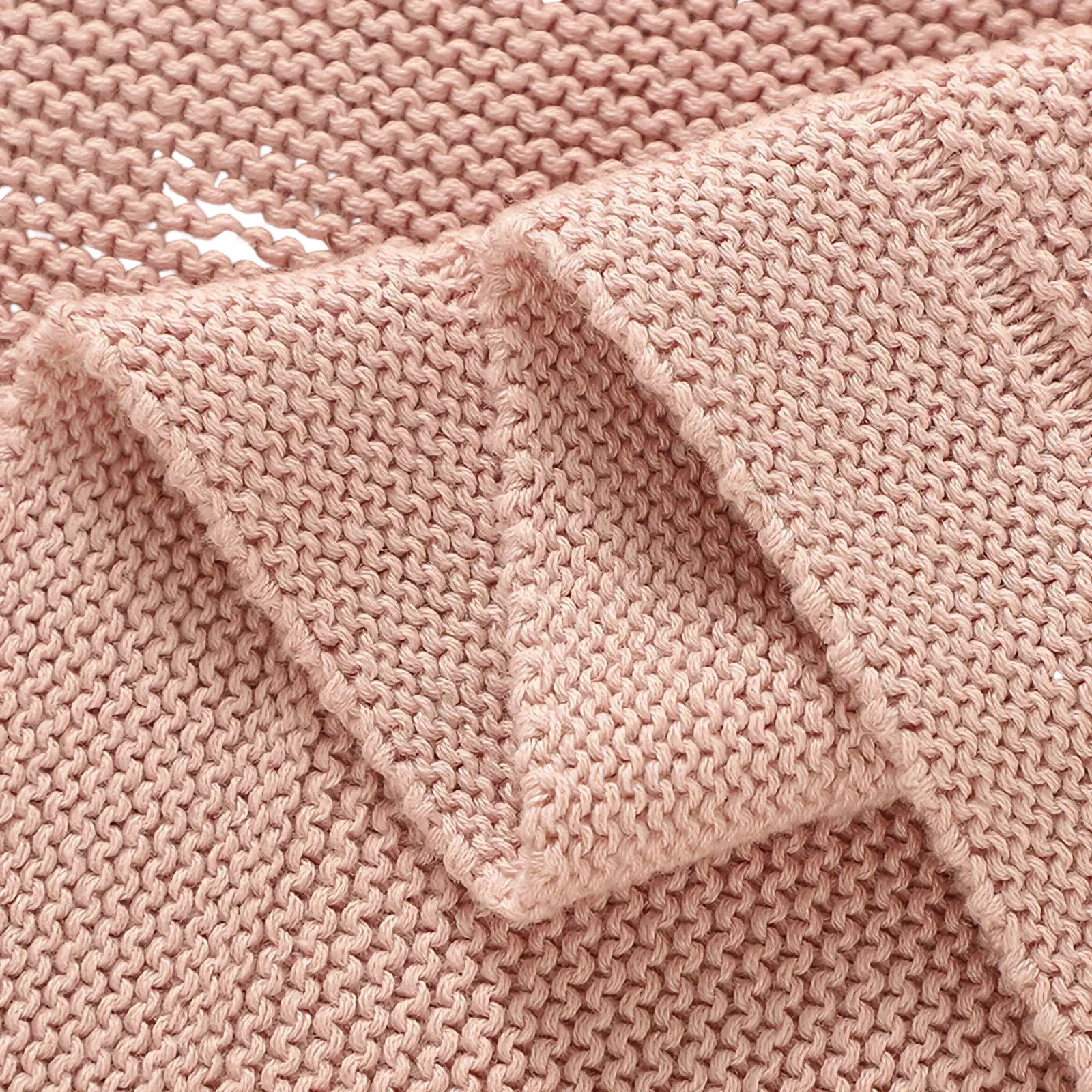 A blush pink knitted baby blanket made of cotton with a consistent textured stitch pattern for receiving use