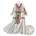 A white bohemian embroidered V-neck maxi dress with colorful floral and geometric patterns in red blue green yellow and purple thread