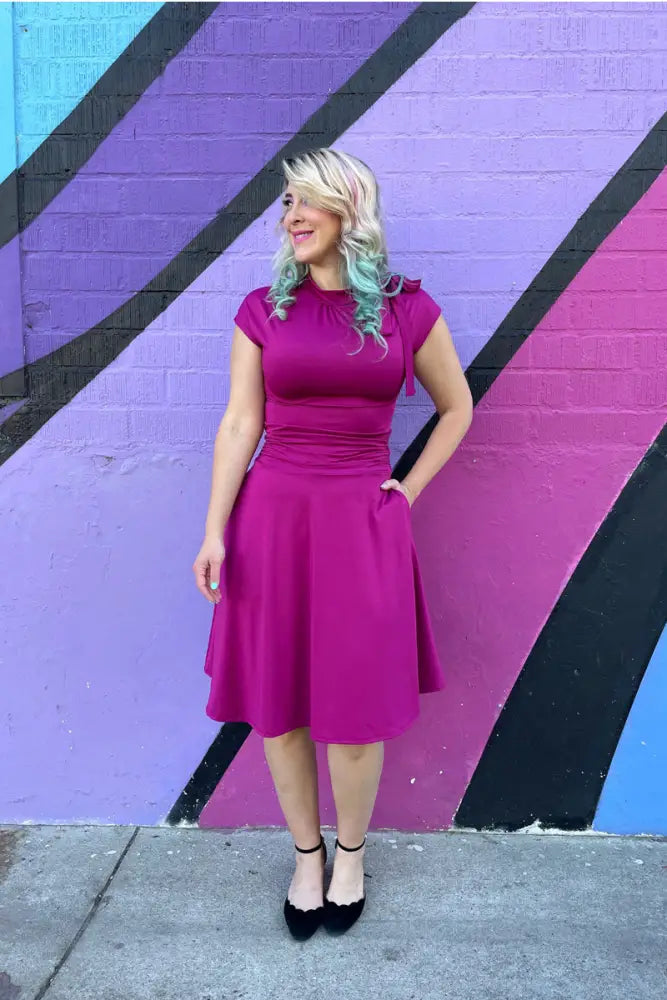 A vibrant magenta ruched a-line bombshell dress with short sleeves fitted bodice and pockets knee-length