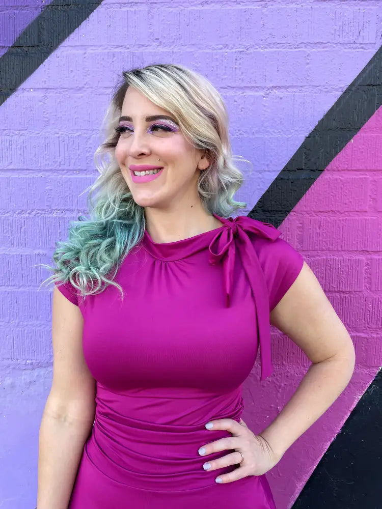 A vibrant magenta ruched a-line bombshell dress with short sleeves decorative bow at the neckline and pockets