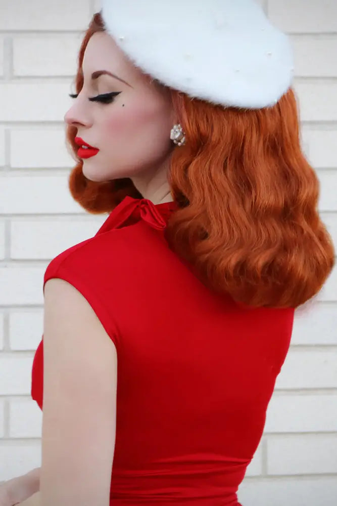 A woman wears a vibrant red retro plus size bombshell dress with bow neckline and pockets paired with a white beret