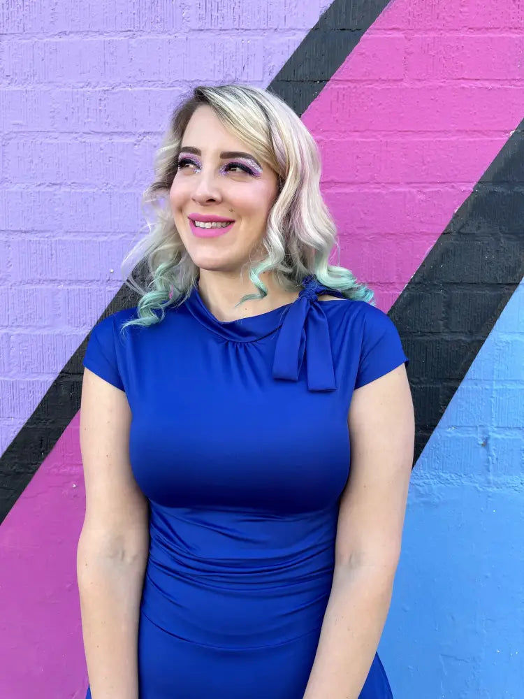A royal blue retro ruched bombshell fitted dress with a decorative bow at the neckline and pockets