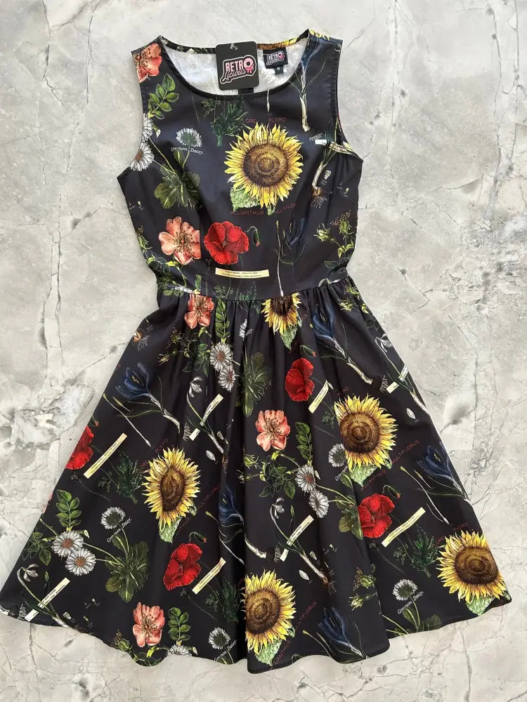 Black sleeveless cotton dress with vibrant yellow, red, pink, and white botanical print featuring sunflowers, poppies, and dandelions
