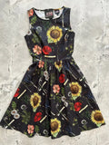 Black sleeveless cotton dress with vibrant yellow, red, pink, and white botanical print featuring sunflowers, poppies, and dandelions