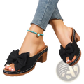 Black bow platform mules with wooden block heels and white stitching in a bow platform mules block heel sandals design