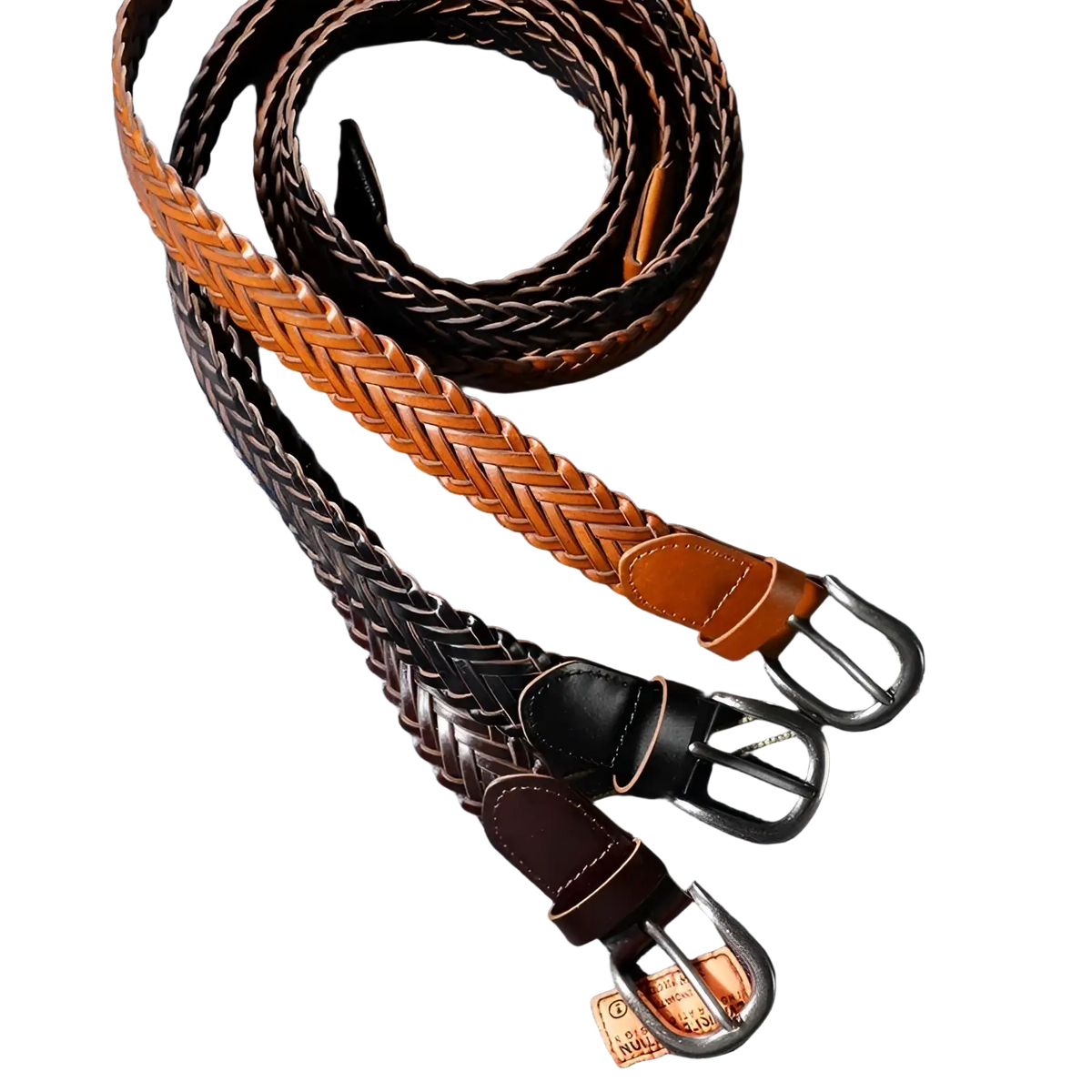 Three braided leather belts in tan black and brown tones with metal buckles lie coiled on denim fabric