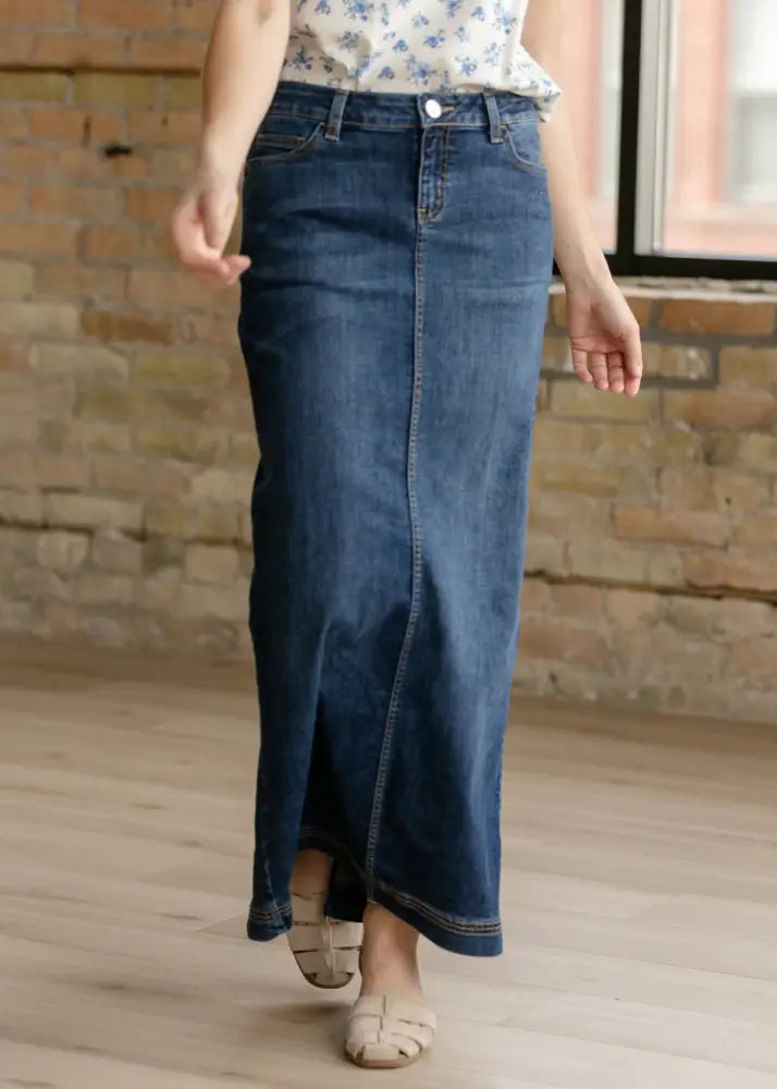 A dark blue denim maxi skirt with a straight cut and side slit made from dark wash denim fabric