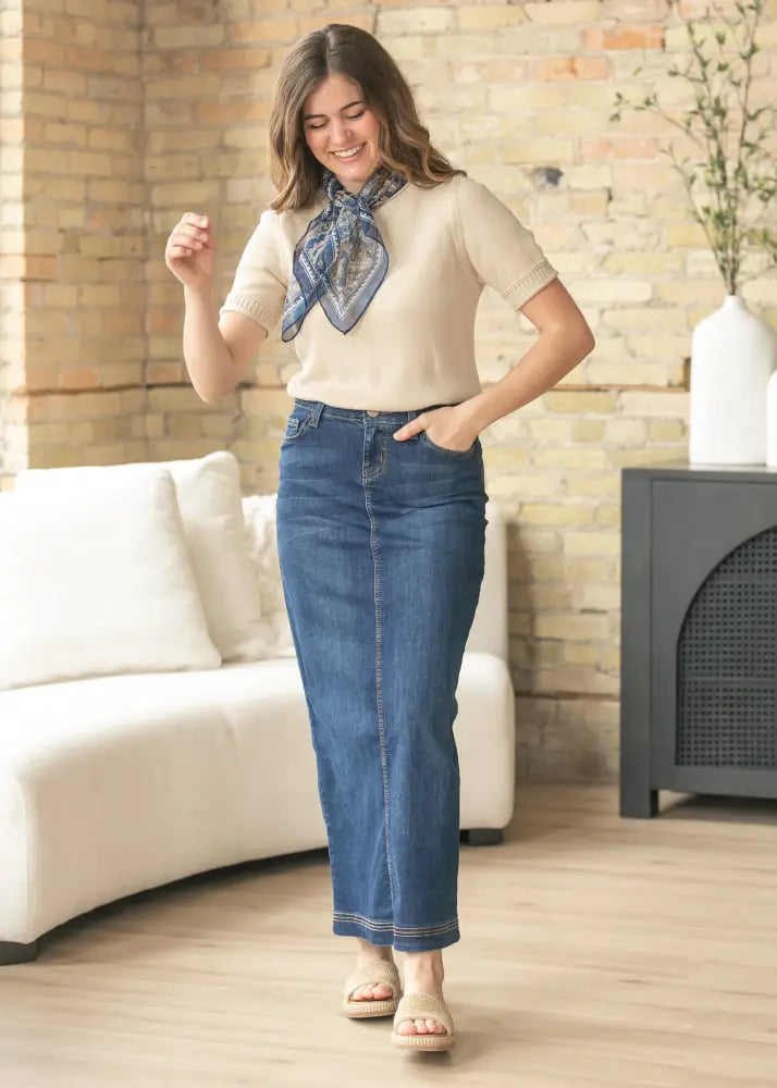 A woman wearing classic blue denim straight-leg jeans with frayed hem and stitching detail in bria dark wash denim maxi skirt with side slit