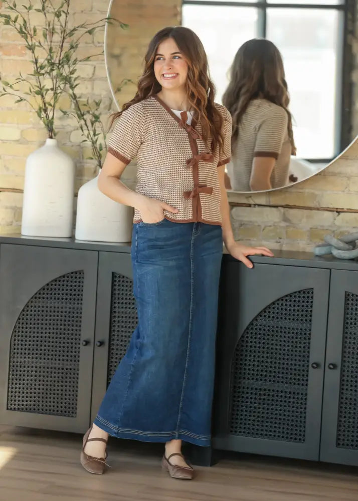 Woman wearing a beige patterned cardigan with toggles over white top paired with bria dark wash denim maxi skirt with side slit