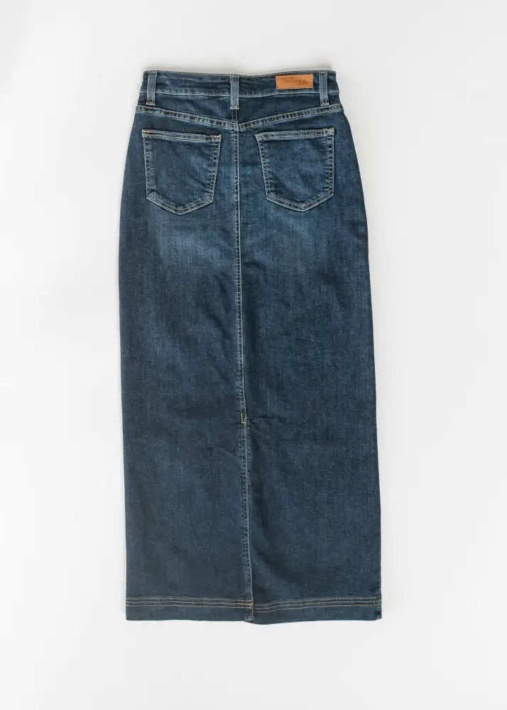 Back view of a bria dark wash denim maxi skirt with side slit featuring two back pockets and a brown leather waistband tag