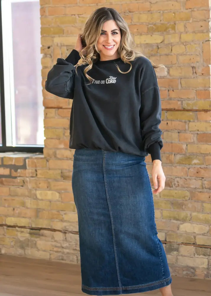 Black long-sleeved sweatshirt with white im on coke graphic paired with bria dark wash denim maxi skirt with side slit