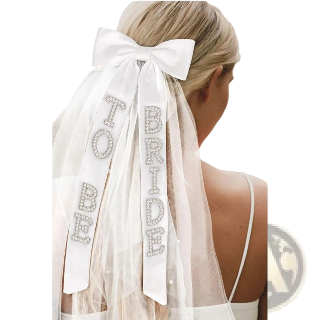 A delicate white bridal bow veil with satin bow and rhinestone bride to be lettering on sheer ribbons