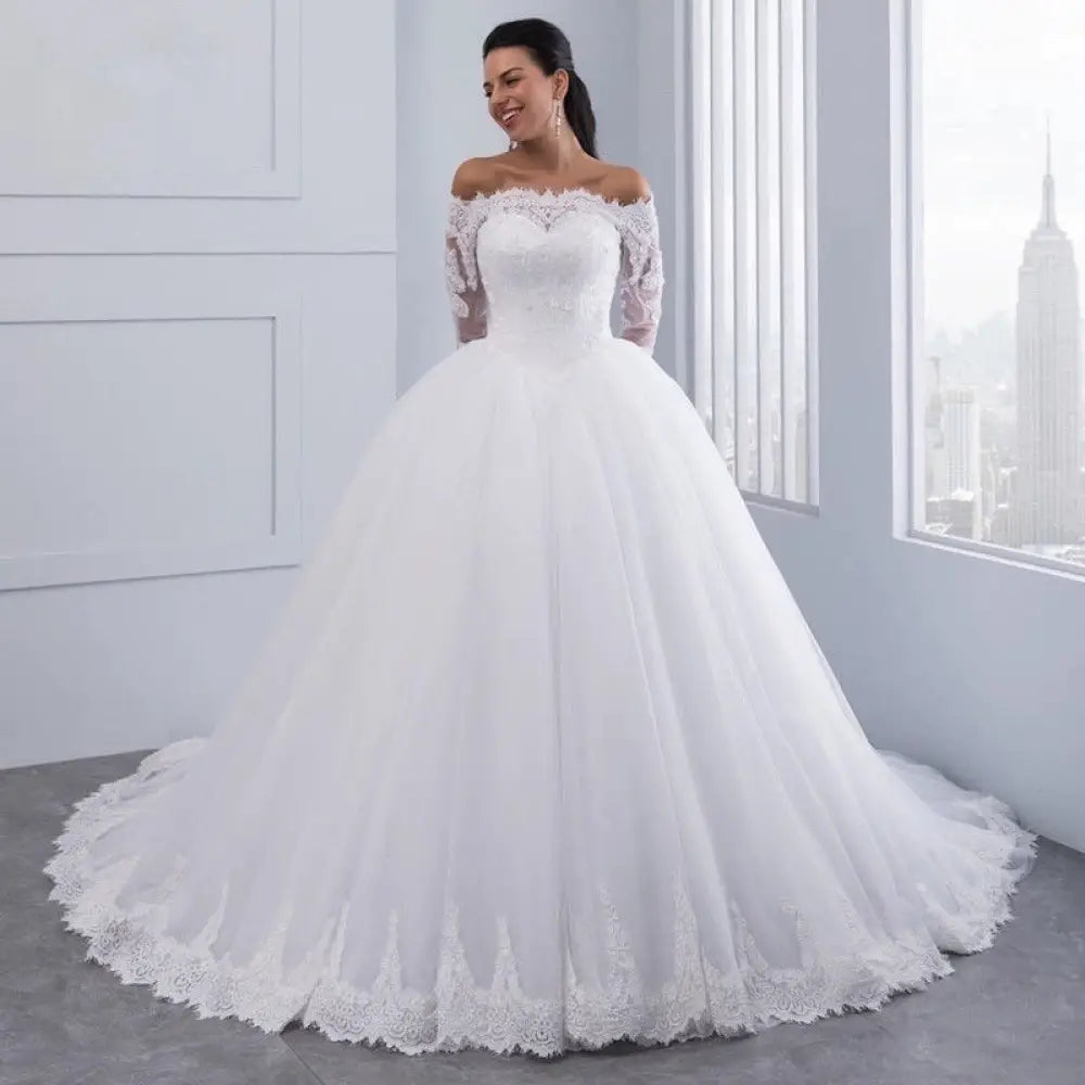 A white off-the-shoulder lace wedding gown with long sleeves and a voluminous tulle skirt for formal occasions