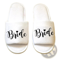 White plush slide sandals with bride printed in black cursive and a heart above the i for bridal shower use