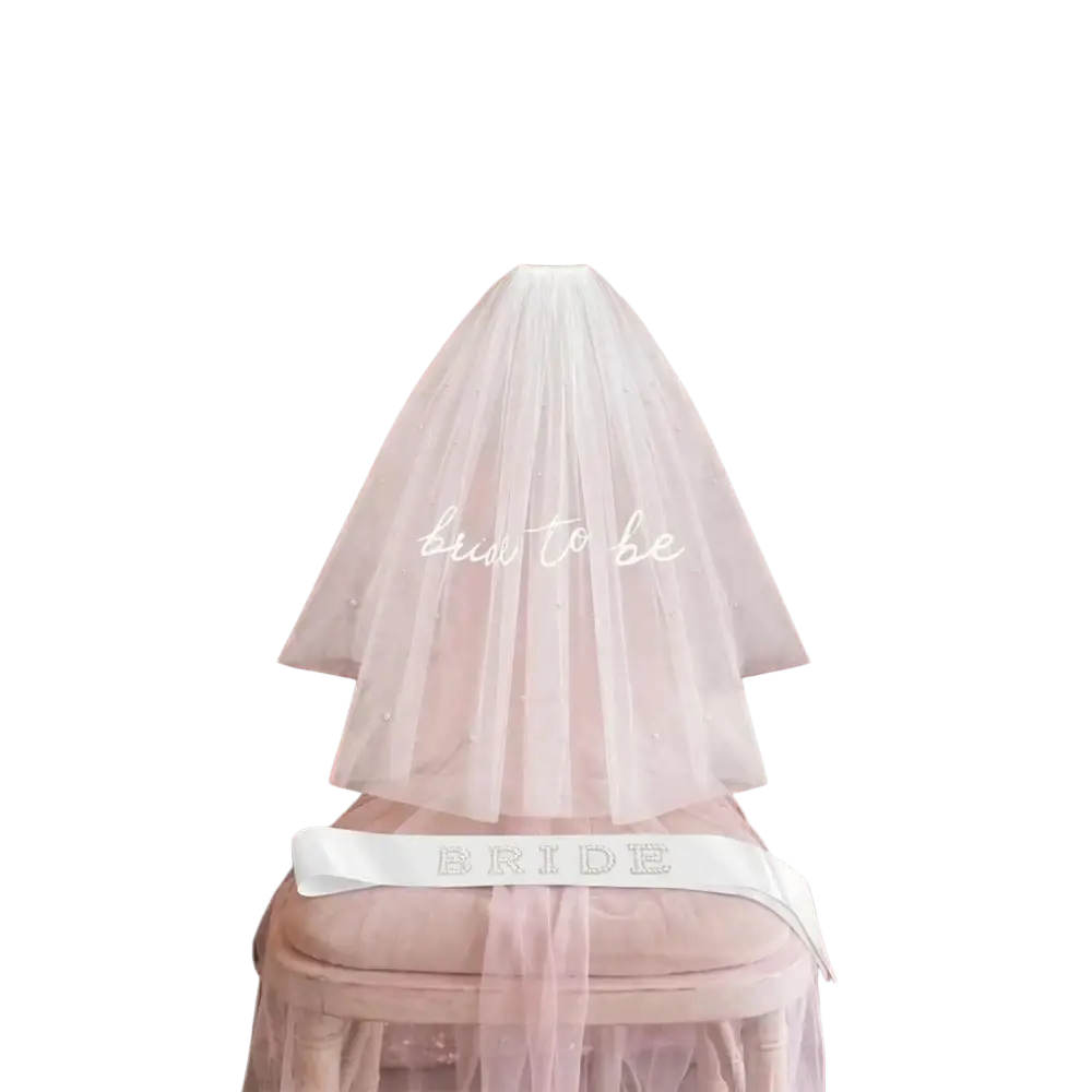 A delicate white tulle veil with subtle beading and embroidered bride to be text draped over a chair