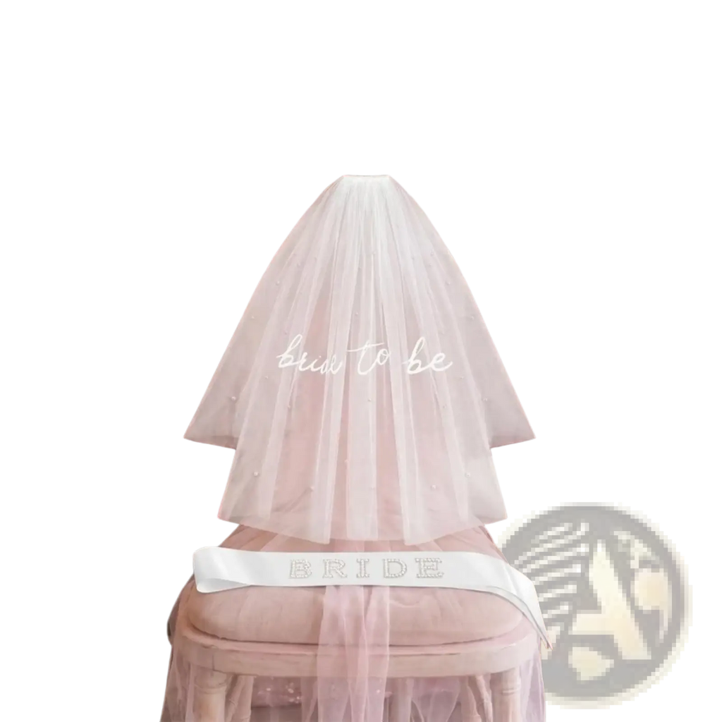 A delicate white tulle veil with subtle beading and embroidered bride to be text draped over a chair