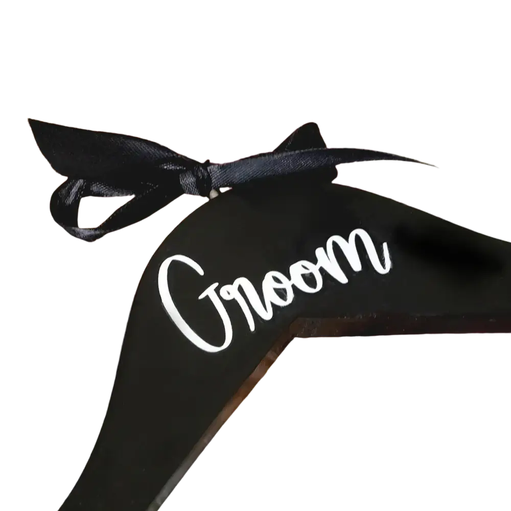 Black wooden groom hanger with white cursive script and black satin ribbon bow from bride and groom pearl wedding hangers set