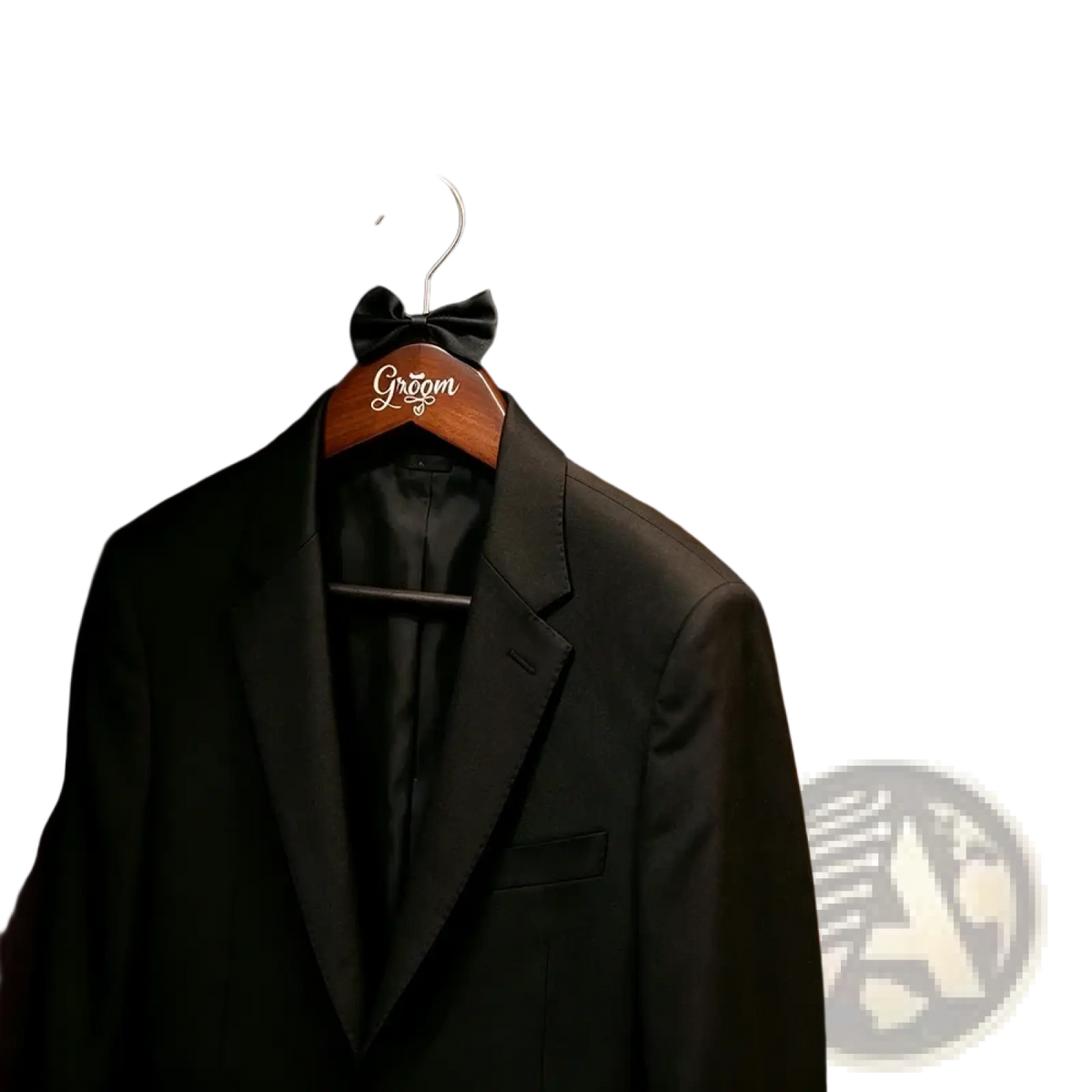 Black tuxedo jacket with black bow tie hanging on a bride and groom pearl wood wedding hanger engraved groom
