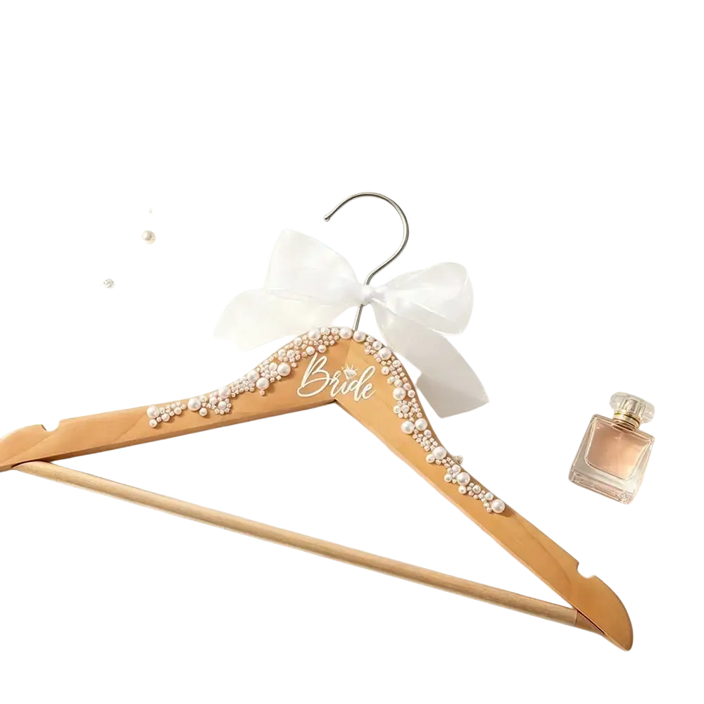 A light wood bride bridal hanger adorned with pearls and a delicate white bow from a wedding hanger set