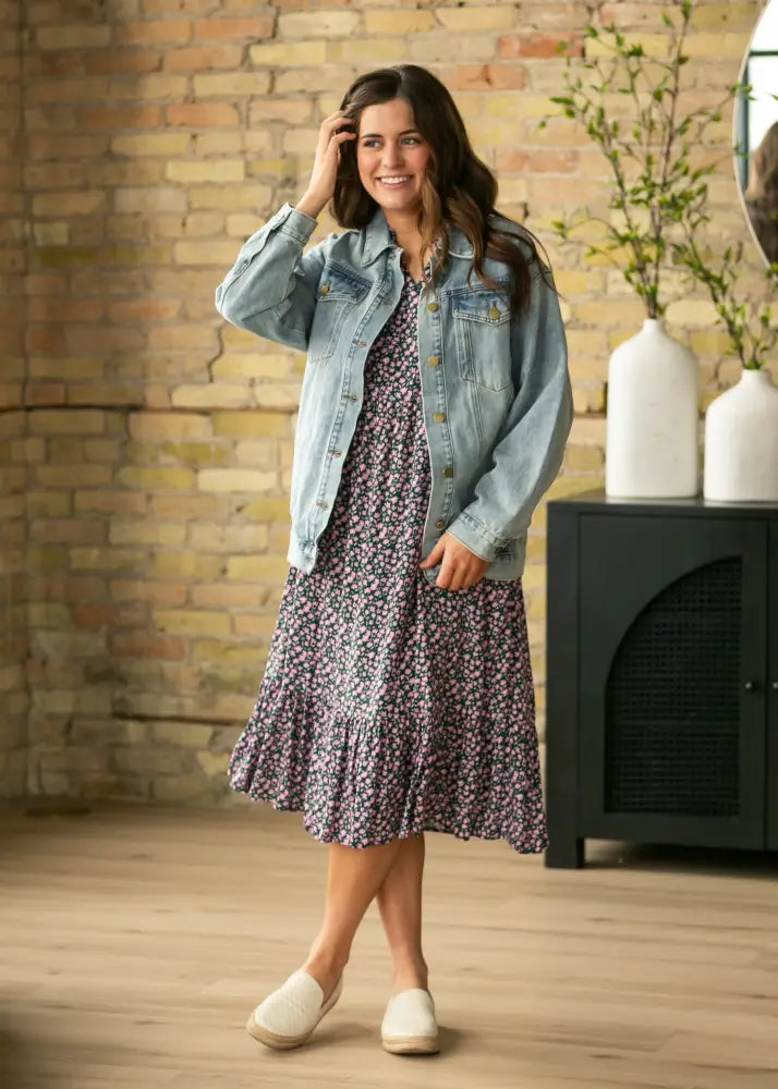 A woman wears a floral print midi dress with ruffled hem under a brinx light wash oversized denim trucker jacket