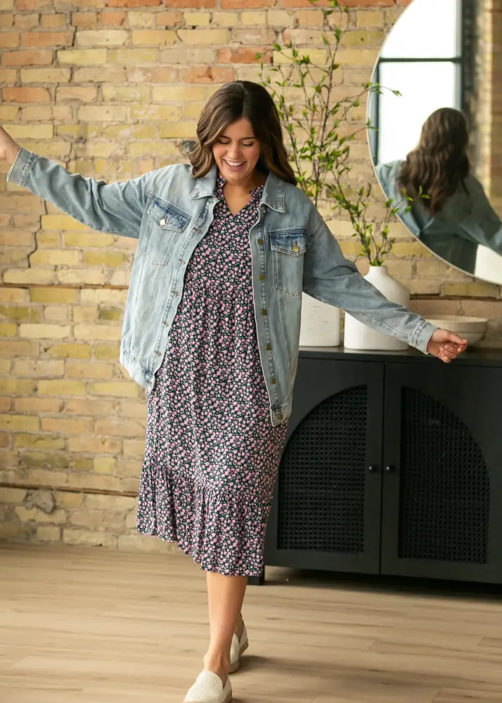 A woman wearing a brinx light wash oversized denim trucker jacket over a navy blue floral midi dress with ruffled hem