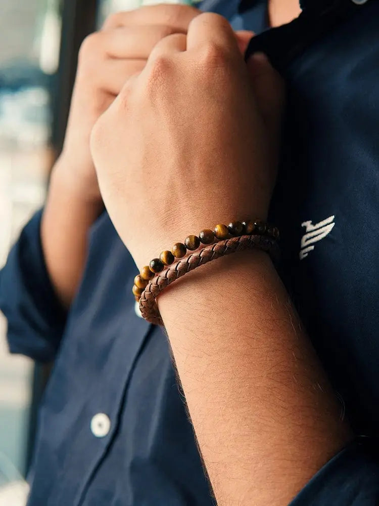 A tiger eye and brown braided leather bracelet with steel clasp worn on a wrist featuring tiger eye beads