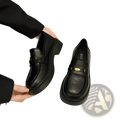Black leather loafers with chunky sole and gold-tone buckle detail creating a bold and stylish look