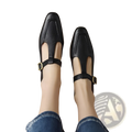 Black leather t-strap flats with gold-tone buckle accents featuring a square toe and mary jane style