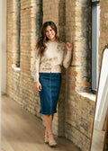 A woman wears a bryn dark wash straight denim midi skirt paired with a cream knit sweater with green leaf embroidery
