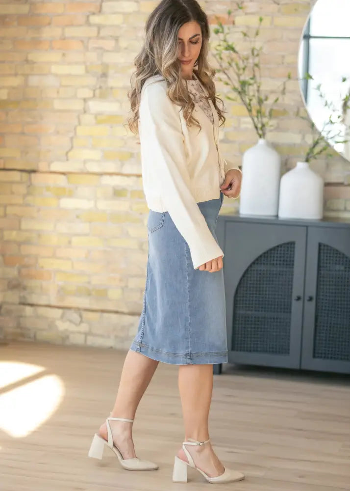 A woman wears a bryn light wash sustainable denim midi skirt in light blue with a front seam and side pockets