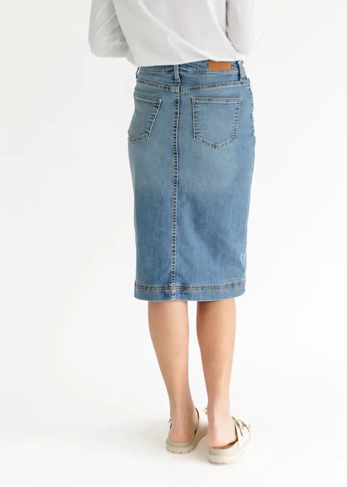 Back view of bryn light wash sustainable denim midi skirt in light blue with two pockets and brown leather patch